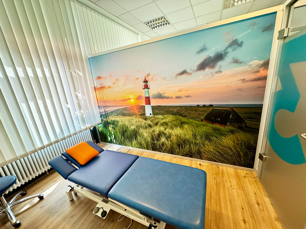 Entspannender Therapieraum der Physiotherapie Dennis Mann Mannheim mit komfortabler Behandlungsliege und beruhigendem Wandbild eines Leuchtturms am Meer.