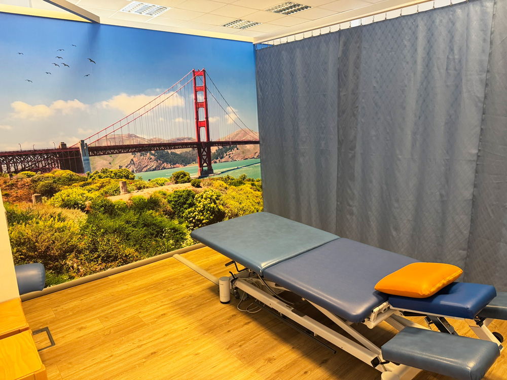Therapieraum der Physiotherapie Dennis Mann Mannheim mit komfortabler Behandlungsliege und einem Wandbild, das die Golden Gate Bridge in San Francisco zeigt.